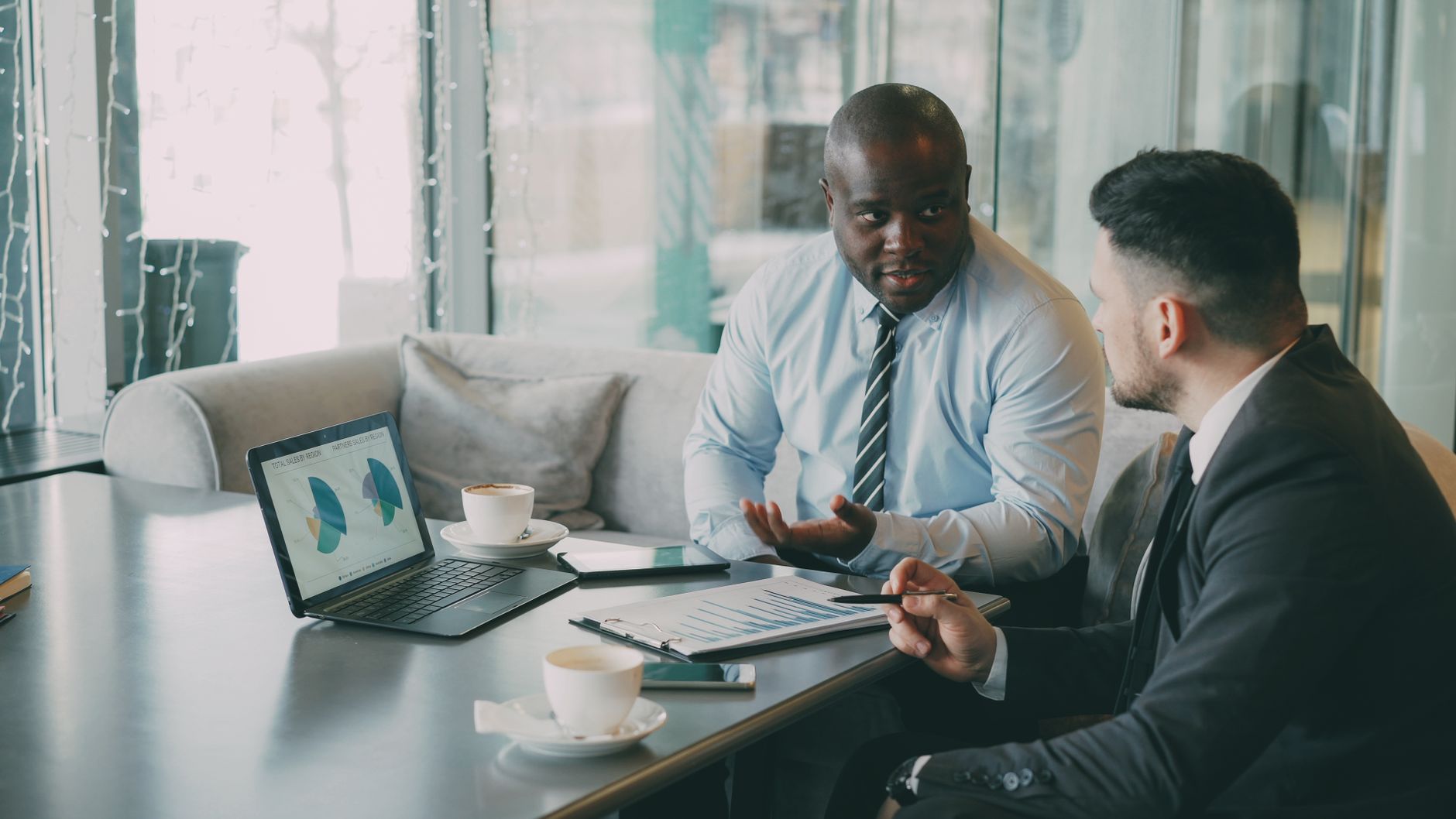 Two business professionals engaged in discussion over laptops and documents. — A Guide to the pros of the digital savings acc