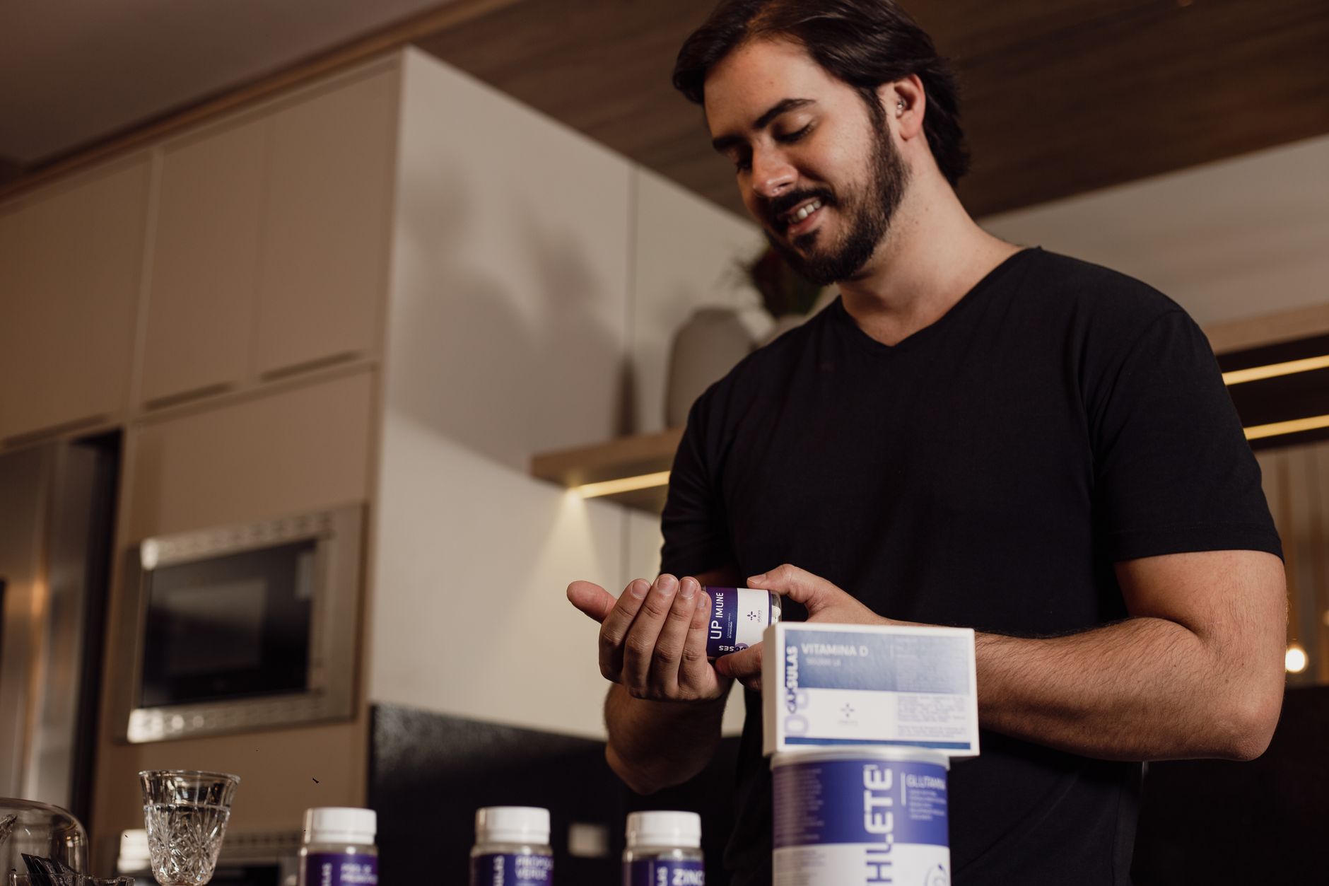 Man in kitchen holding and reviewing a bottle of supplements, indicating health-conscious lifestyle. — Achieve Superior Fitne