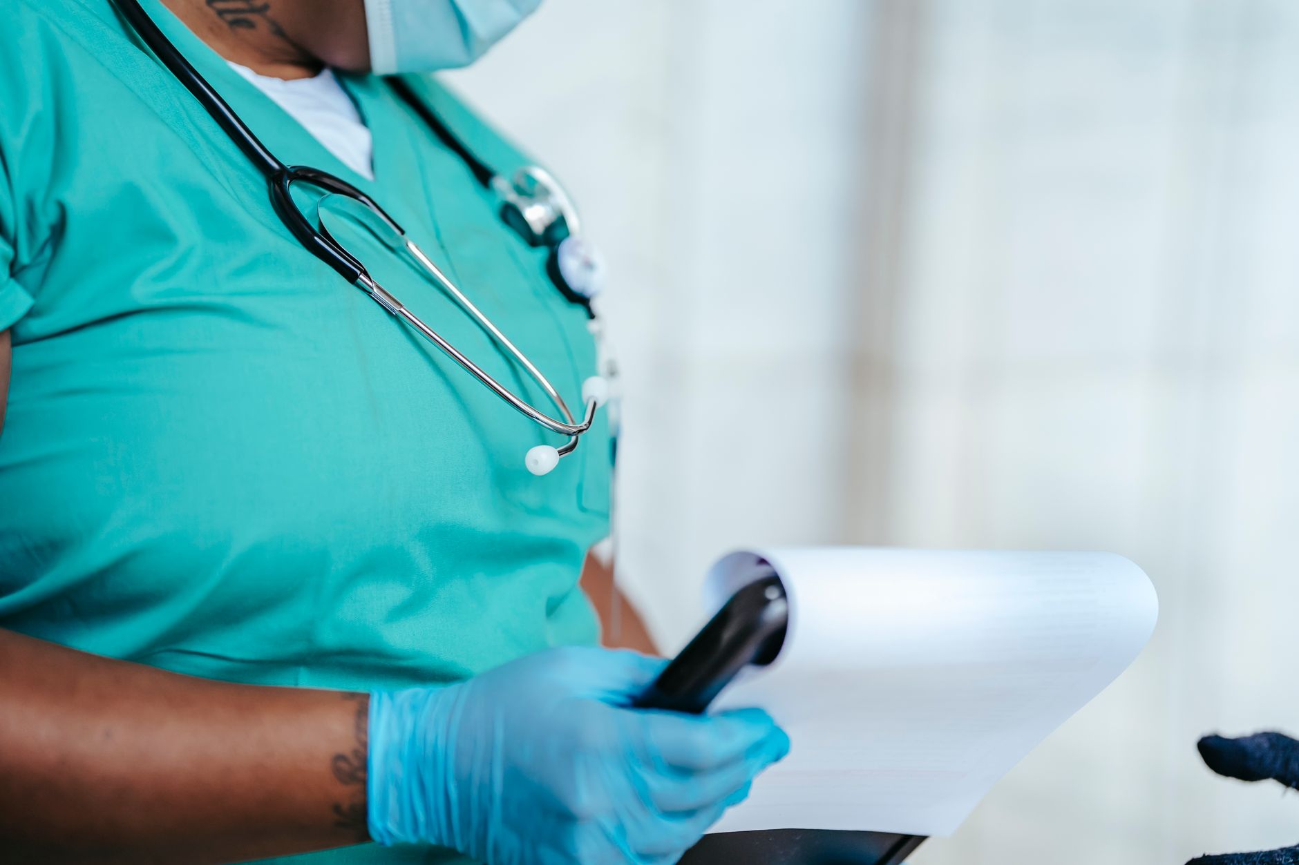 Side view of crop anonymous tattooed ethnic female medic in uniform with stethoscope and papers on clipboard — Dr Scott Kamel