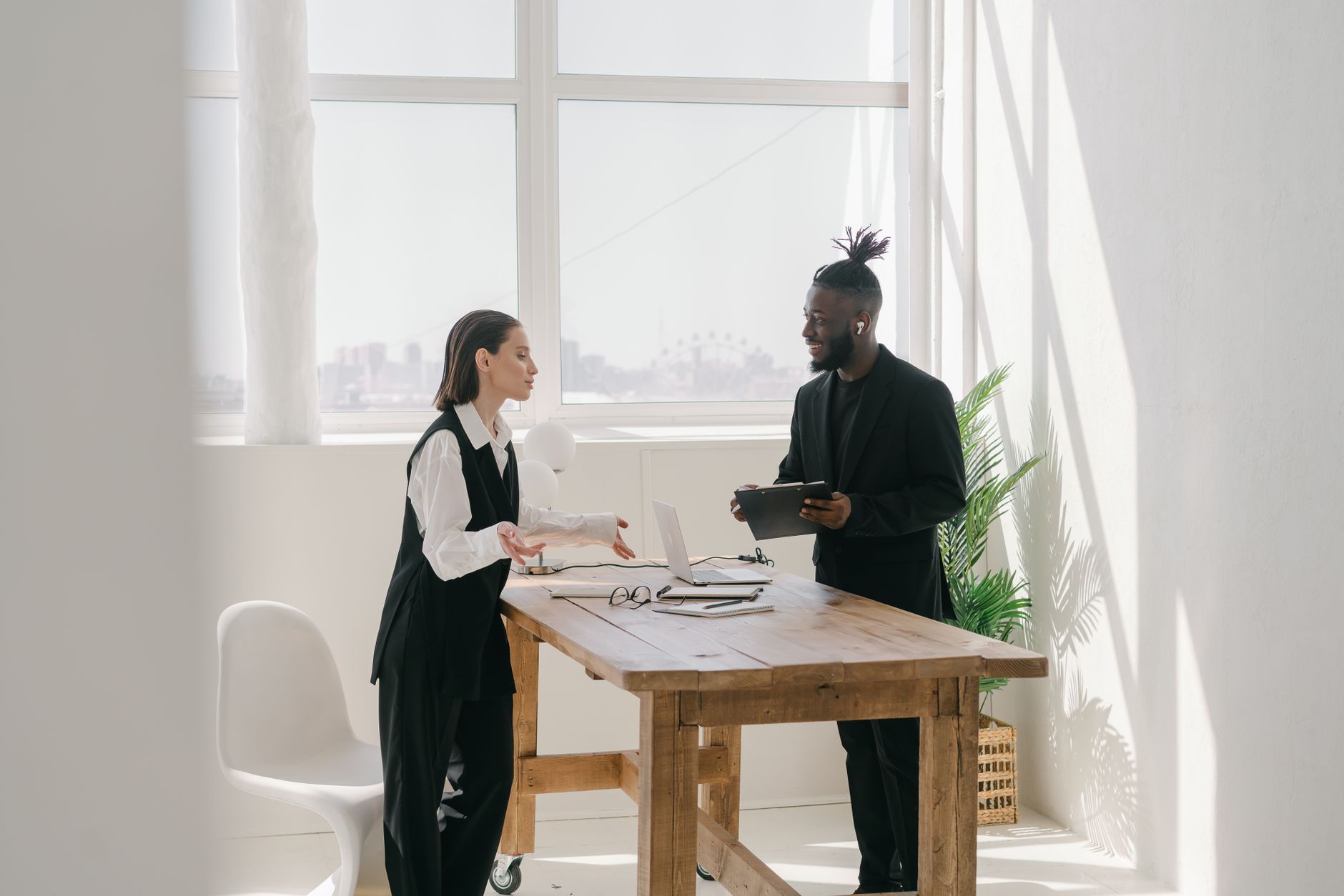 A diverse team engaging in a discussion around a wooden table with natural light filling the modern office space. — Explore H
